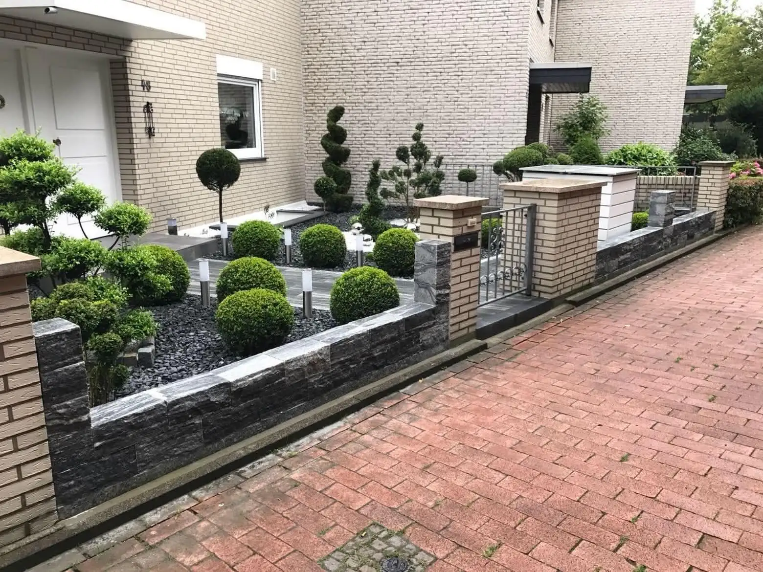 Vorgarten mit Natursteinmauer, Kugelbuchs und Formgehölzen
