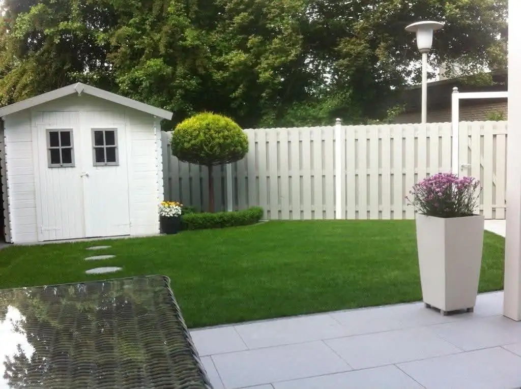 Rasenfläche mit weißem Gartenhaus und Zaun